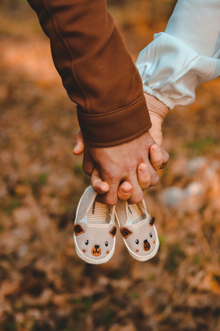 Close-up of hands holding adorable baby shoes amidst autumn leaves, symbolizing family and new beginnings.