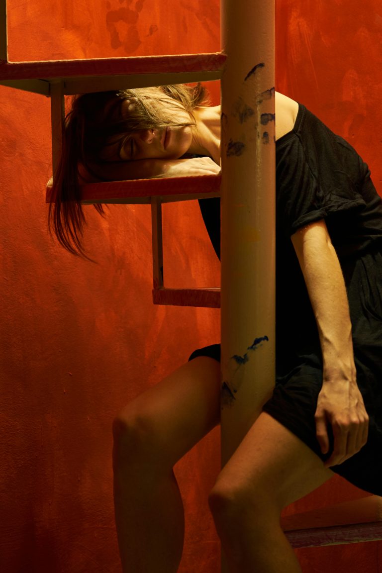 Woman in black dress posing on stairs, red background enhances mood.