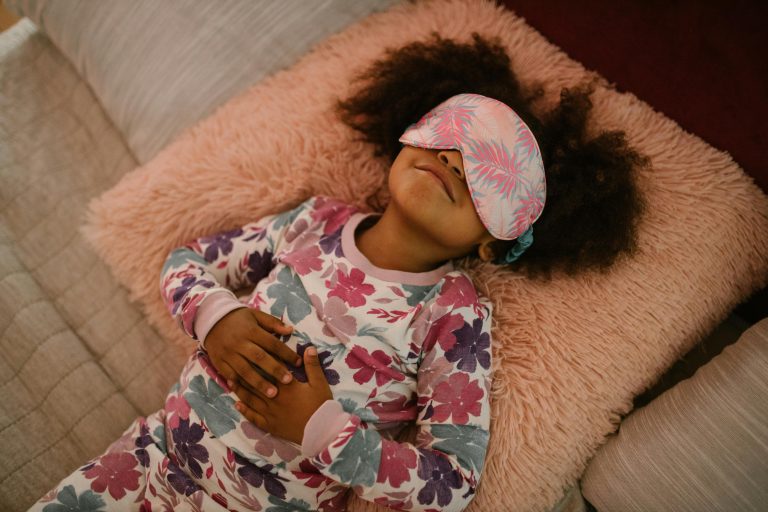 A young girl wearing floral pajamas and sleep mask, resting peacefully on a fluffy pillow.