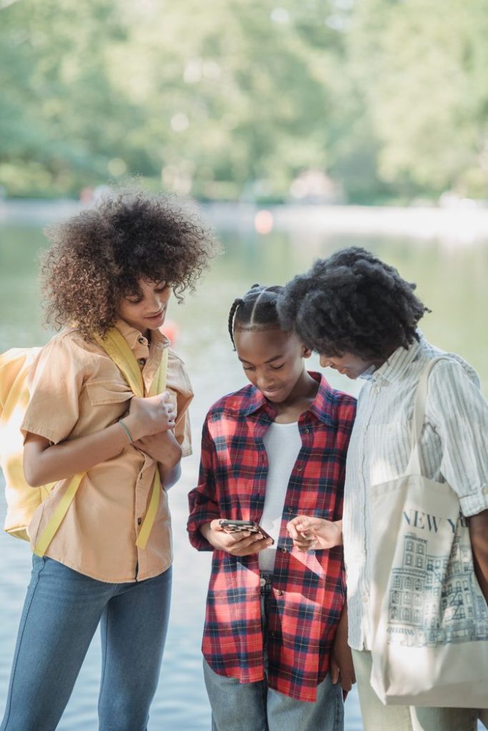 Three people enjoy a sunny day outdoors, sharing moments on a smartphone.
