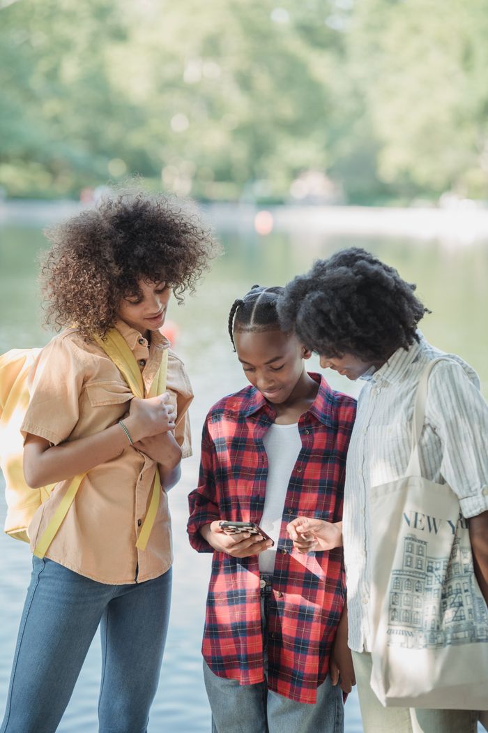 Three people enjoy a sunny day outdoors, sharing moments on a smartphone.