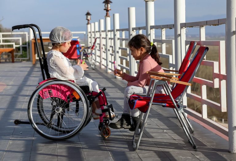 Side view of little girls talking with each other near metal railing with streetlights